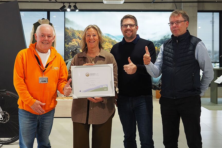 Kalkhoff ist Fahradfreundlicher Arbeitgeber in Gold Vier Personen stehen in einem Ausstellungsraum. Eine Frau hält eine gerahmte Urkunde, zwei Männer zeigen den Daumen nach oben.